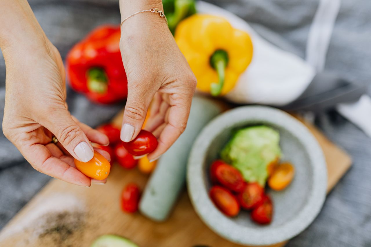 Hands holding fresh cherry tomatoes over a colorful kitchen prep area with various ingredients.