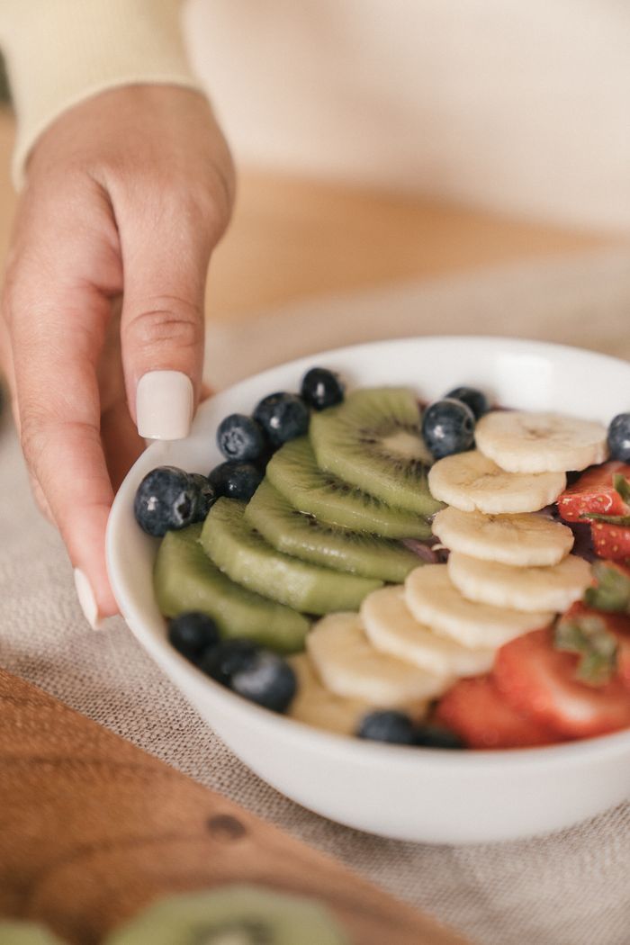 A ceramic bowl filled with fresh sliced kiwi, banana, blueberries, and strawberries, ideal for healthy eating.